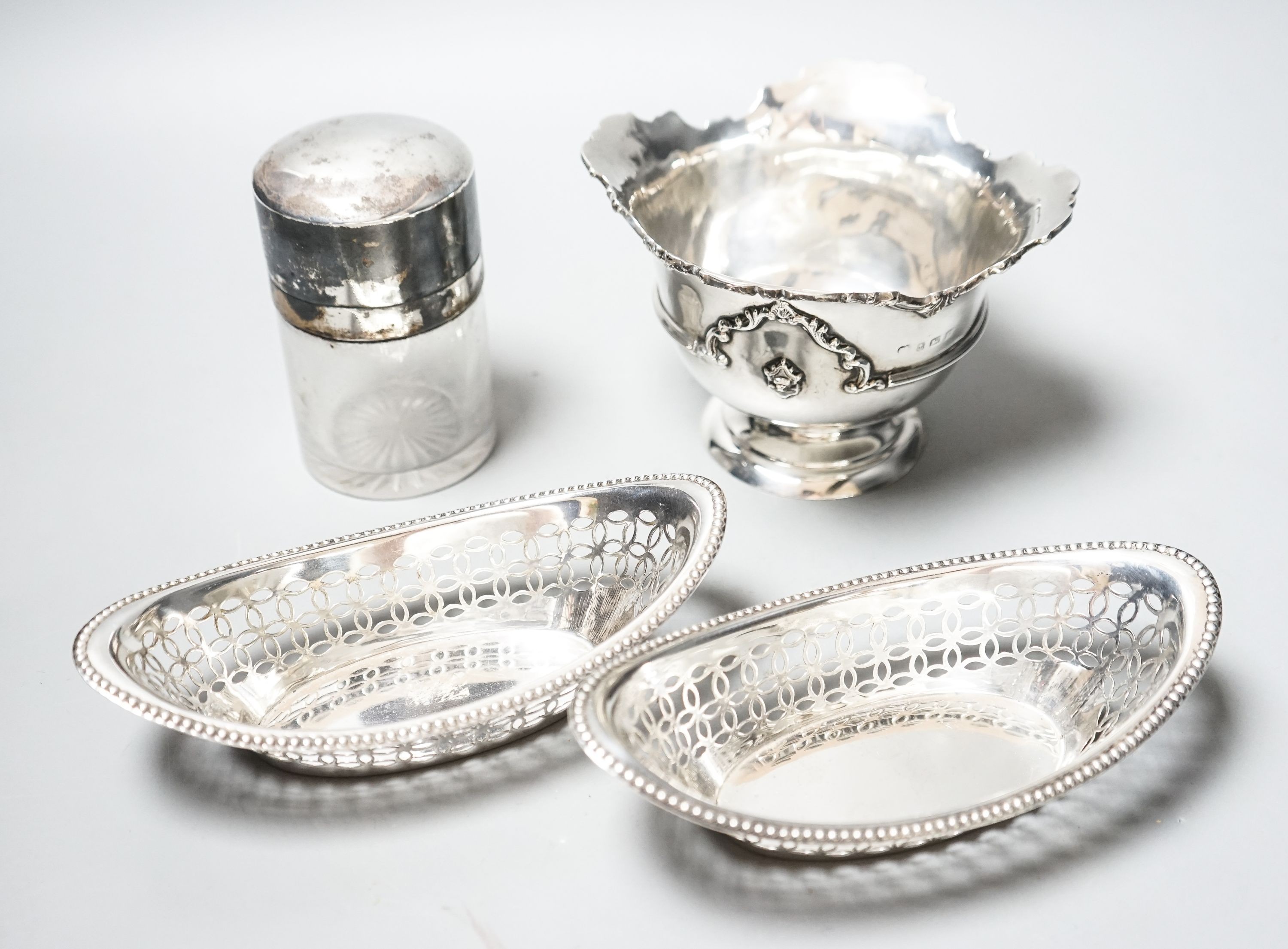 A pair of Edwardian silver oval bon bon dishes, a George V silver sugar bowl and a silver mounted glass smelling salts bottle.